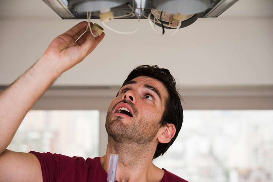 Close-up of male electrician installing holder of ceiling light<br />